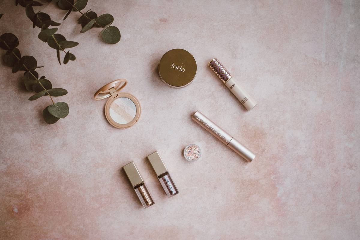 A minimalist clean makeup kit laid out on a marble surface: one tinted moisturizer, one cream blush stick, one retractable brow pencil, one mascara, one tinted lip balm, all in recyclable packaging — clean makeup kit